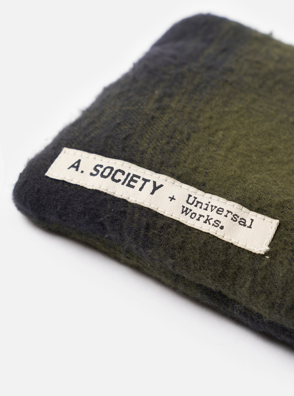 Product shot of the A. SOCIETY x Universal Works Olive Hollywood Sunglasses resting on top of its protective fabric pouch against a plain white studio background, highlighting the olive frame.