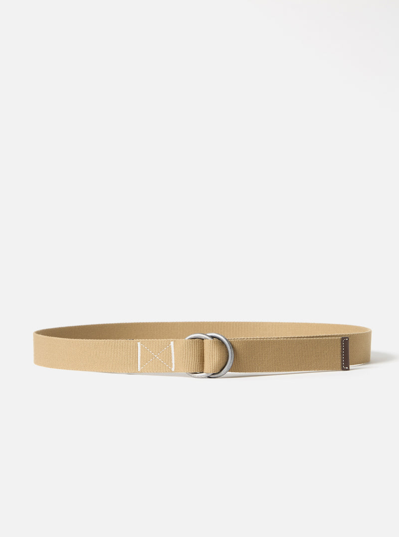 The Sand Canvas Webbing O Ring Belt is shown as a flat lay against a white background. The belt is made from a light beige canvas webbing and features two silver-toned O-ring buckles at one end. The end of the belt is finished with a brown leather trim.