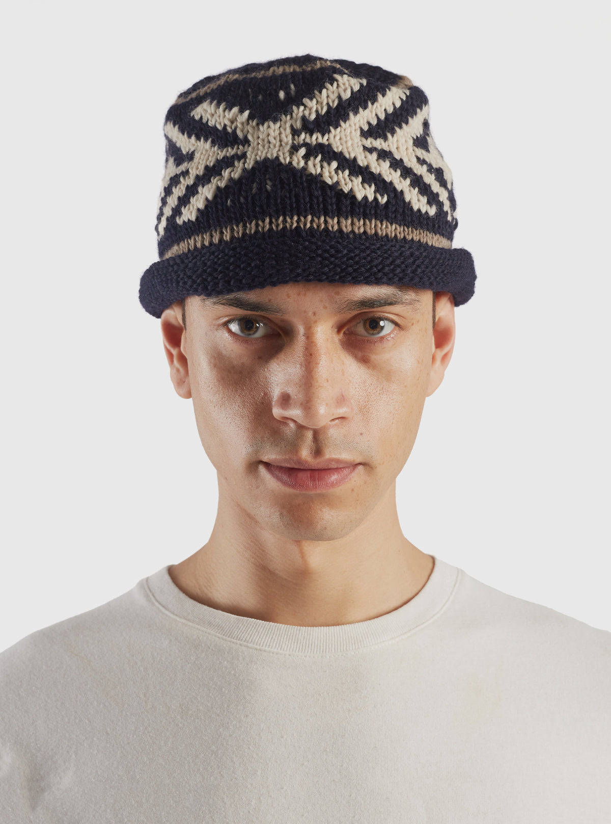 A full studio product view of the cableami® Navy Wool Jacquard Watch Cap set against a plain white background, highlighting its folded cuff, ribbed brim, and intricate jacquard-knit pattern throughout the crown.