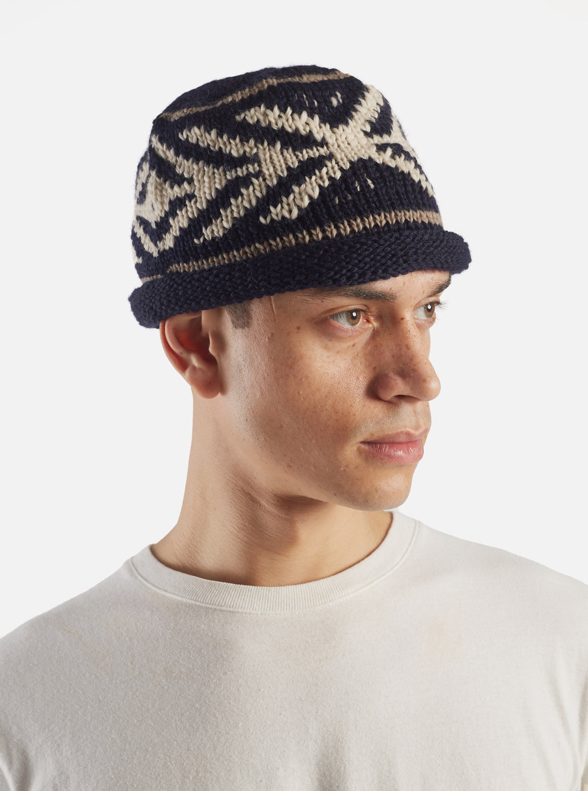 An angled side product shot of the cableami® Navy Wool Jacquard Watch Cap on a plain white background, showcasing the knit structure, turn-up rim, and subtle pattern texture around the crown.