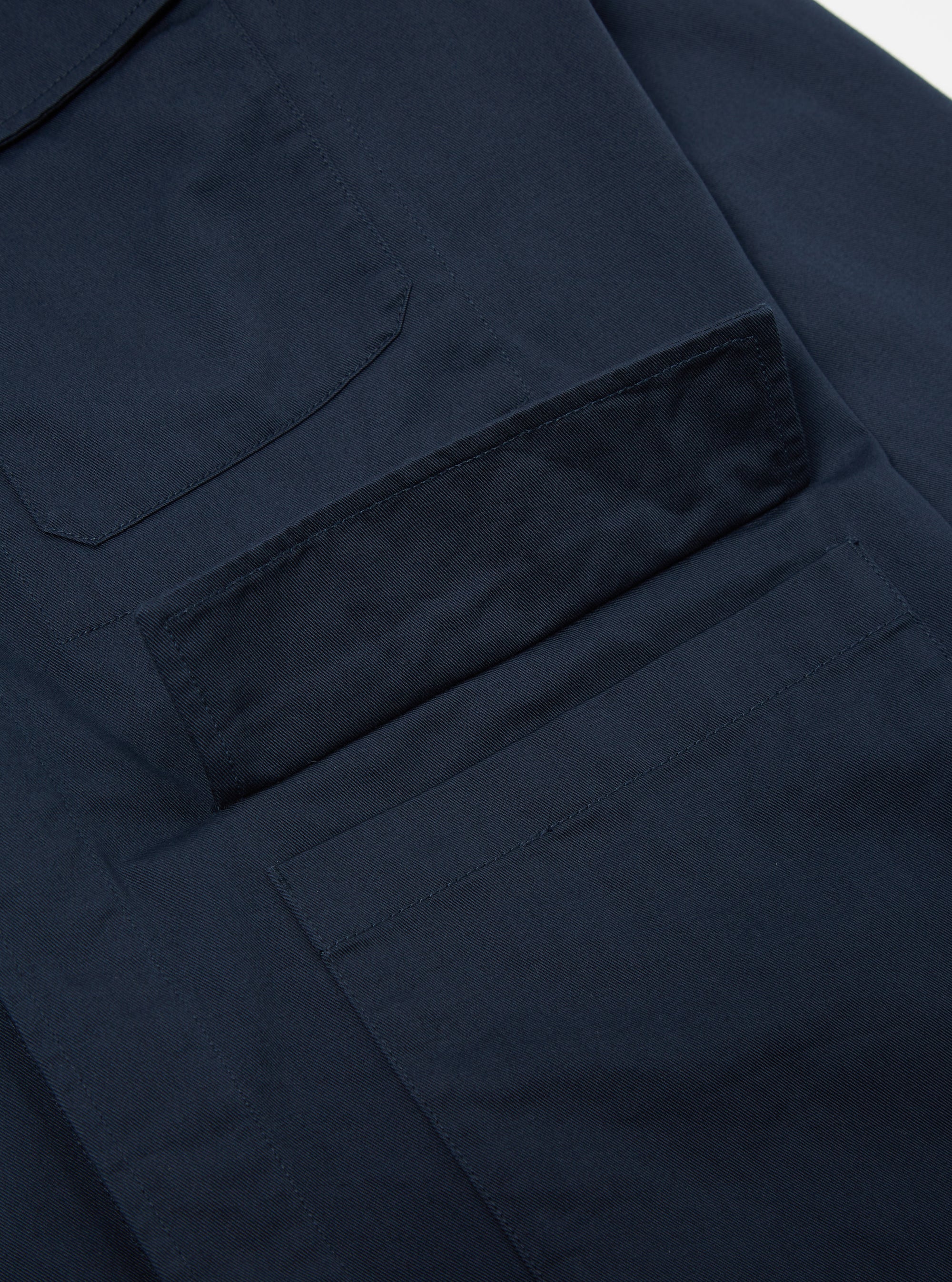 Close up of the Navy Twill MW Fatigue Jacket showing the twill fabric and pocket detail. The jacket is laid on a white surface.
