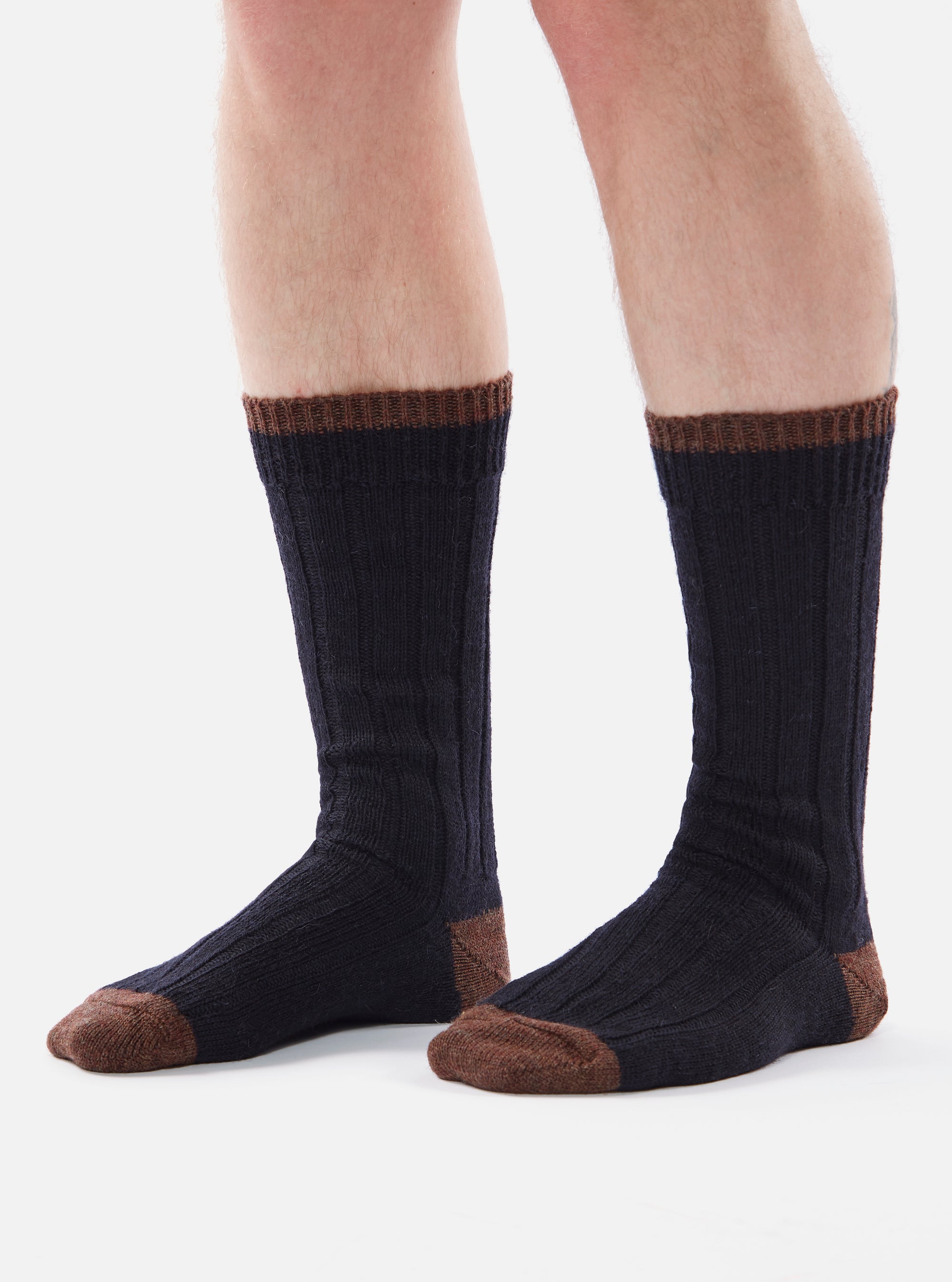 Close-up of a model's legs wearing navy wool hike socks with brown toe and cuff on a white background.