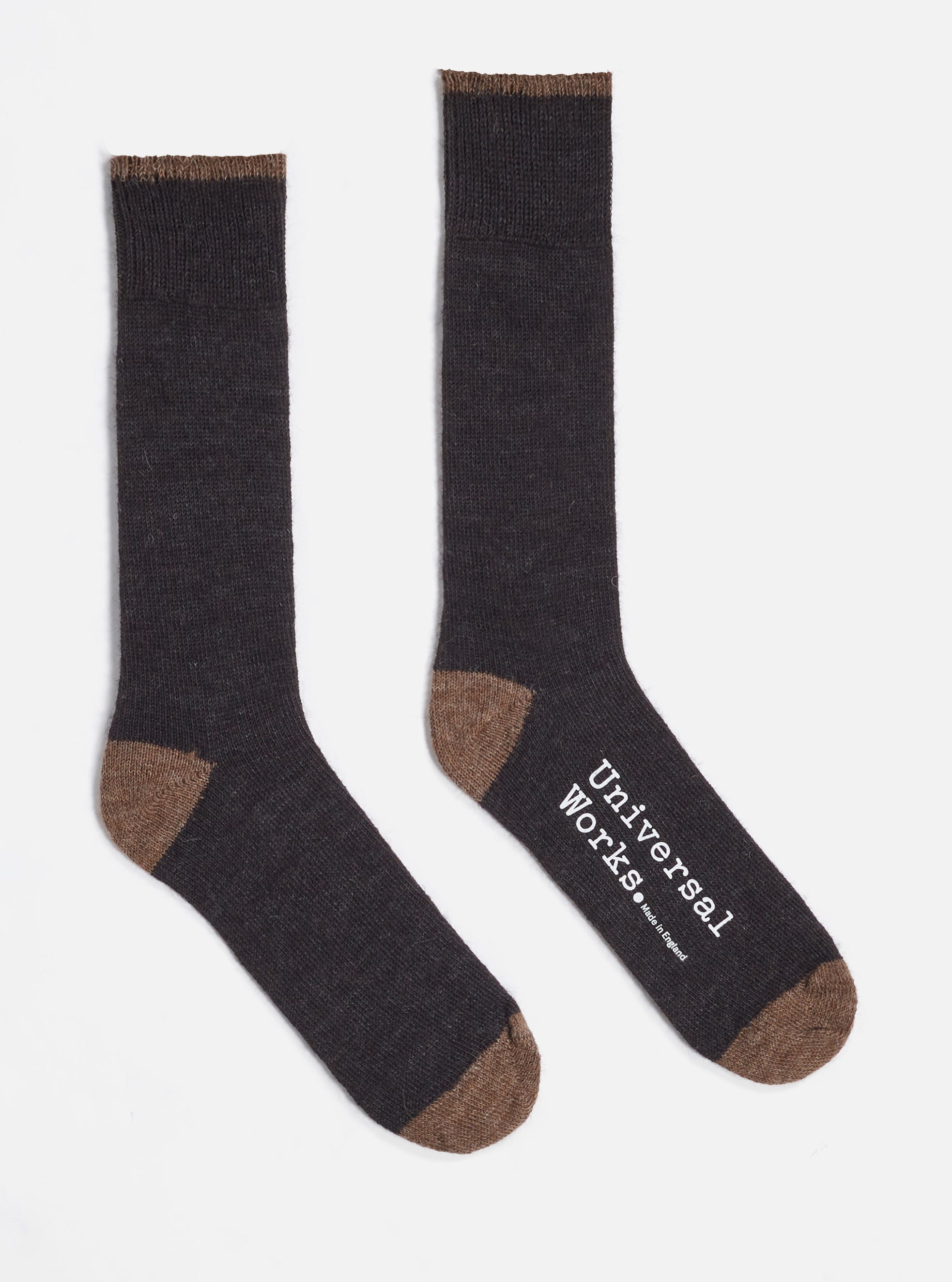 Two Charcoal Alpaca Wool Sock on a white background. The socks are charcoal with brown toes and cuffs. One sock has the words "Universal Works. Made in England" printed on it.