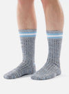 A person stands on a white background wearing Cornish Blue Cotton Everyday Stripe Sock. The socks are striped with white and light blue at the top.