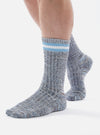 Close up of a model wearing Cornish Blue Cotton Everyday Stripe Sock on a white background. The sock is blue with white and light blue stripes at the top.