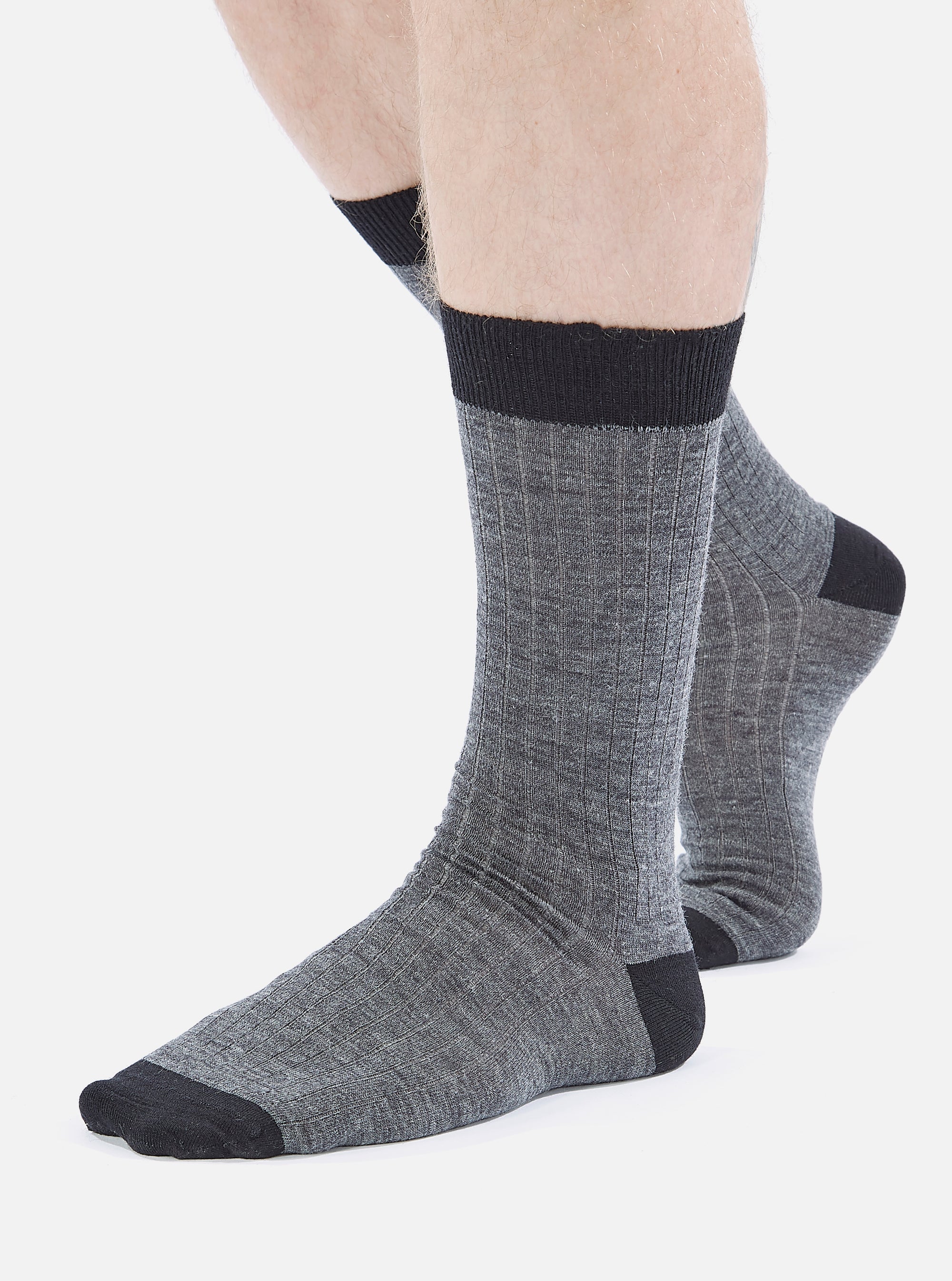 A model wears Grey Marl Merino Classic Sock, made of merino wool. The socks are grey with black toe and top. The background is a plain white.