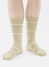 A person wearing Dark Sand Tie Dye Knit Slub Sock. The socks are tan with white stripes, knit material, on a white background.