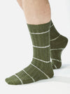 Close-up of a model wearing Olive Tie Dye Knit Slub Socks. The olive green socks feature white stripes and a ribbed texture. Shot against a bright white backdrop.