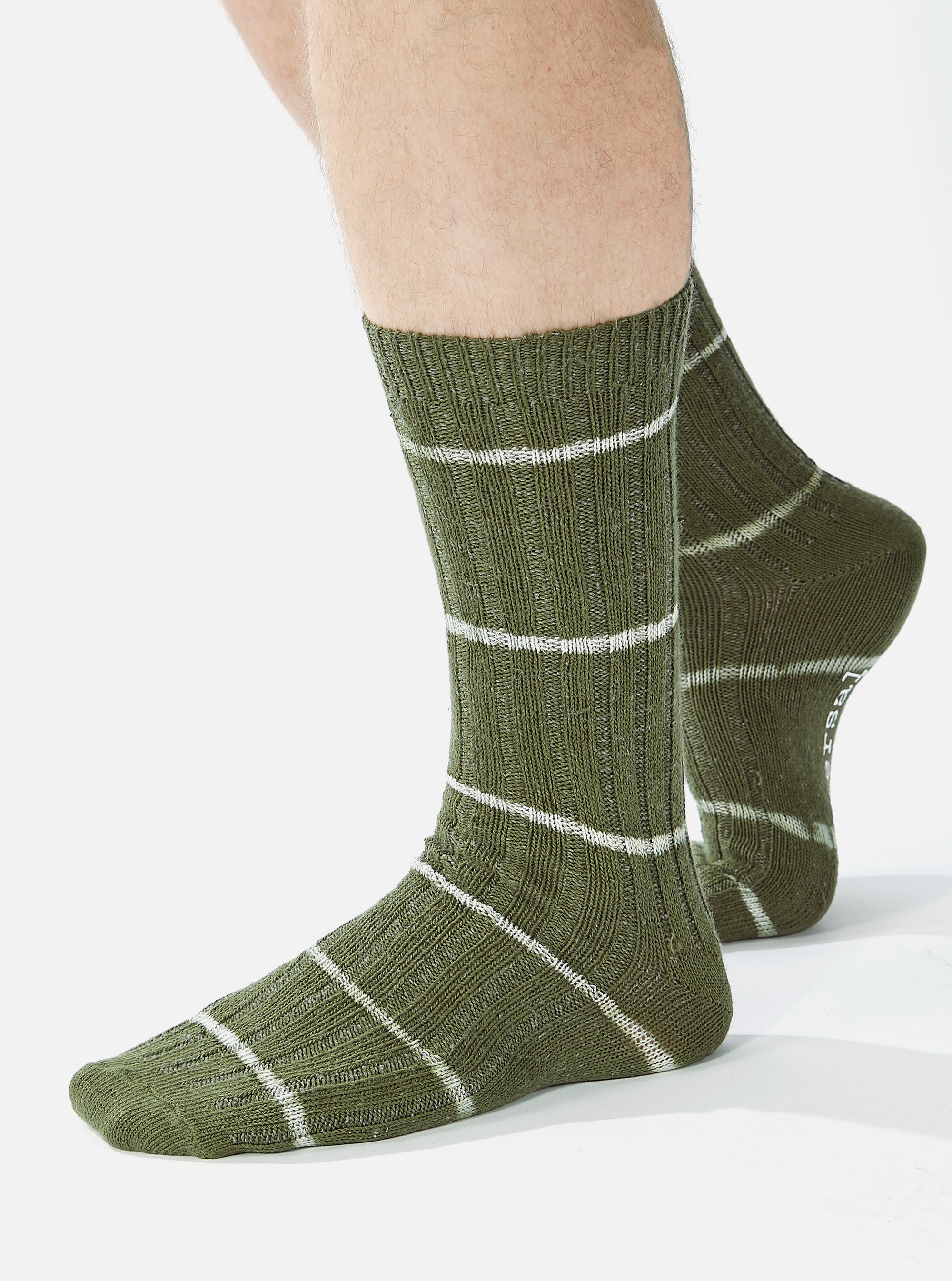 Close-up of a model wearing Olive Tie Dye Knit Slub Socks. The olive green socks feature white stripes and a ribbed texture. Shot against a bright white backdrop.