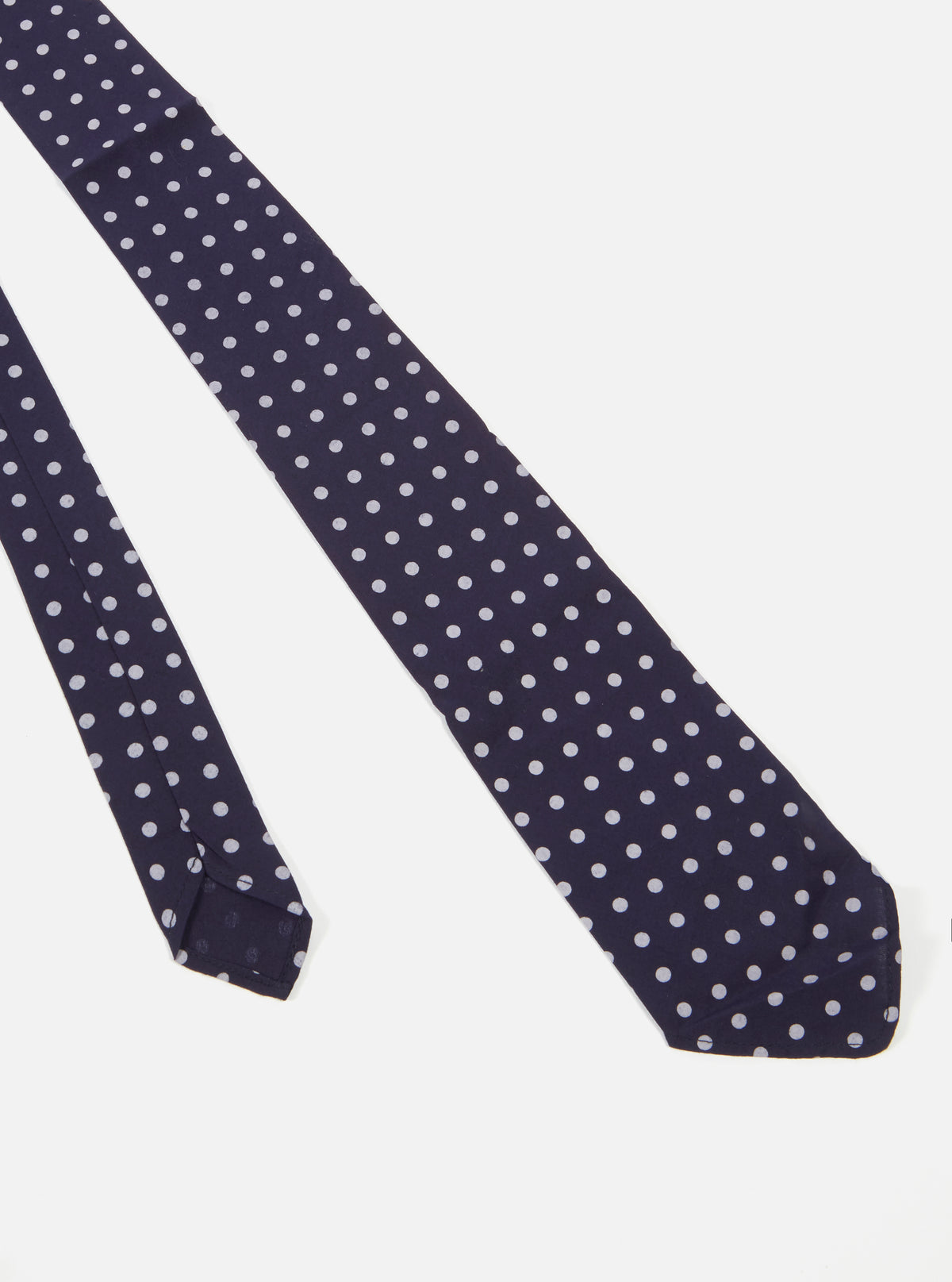 Close-up of a Navy Dot Print Tie on a white background. The tie is navy with white polka dots. The fabric has a slight sheen.
