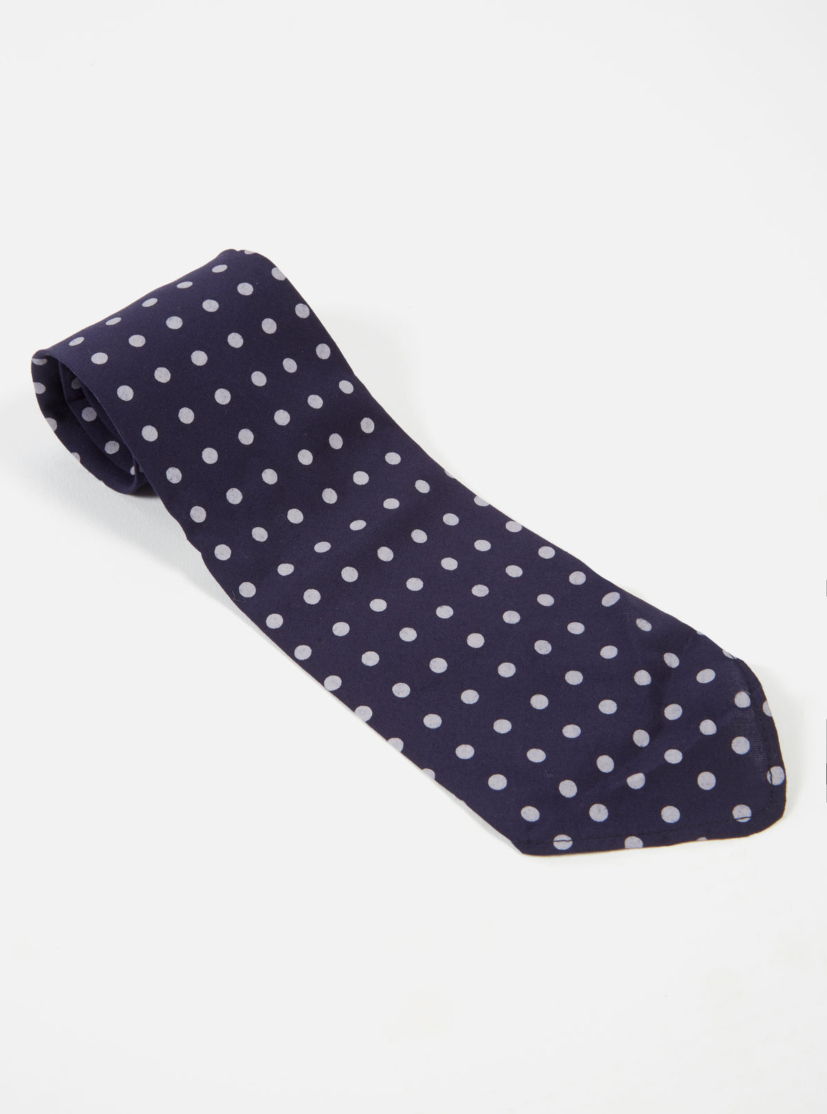 Close-up of a Navy Dot Print Tie on a white surface. The tie is navy blue with white polka dots. The fabric has a smooth, slightly shiny appearance.