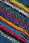 Close-up of the Hanami of Rome Bandana Necklace/Bracelet #5. Braided strips of colorful bandana fabric (red, blue, yellow, black, white) are arranged diagonally on a denim background.