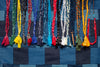 Close-up of Hanami of Rome Bandana Necklace/Bracelet #5 on a blue patchwork denim background. Braided strands in red, yellow, blue, and black.
