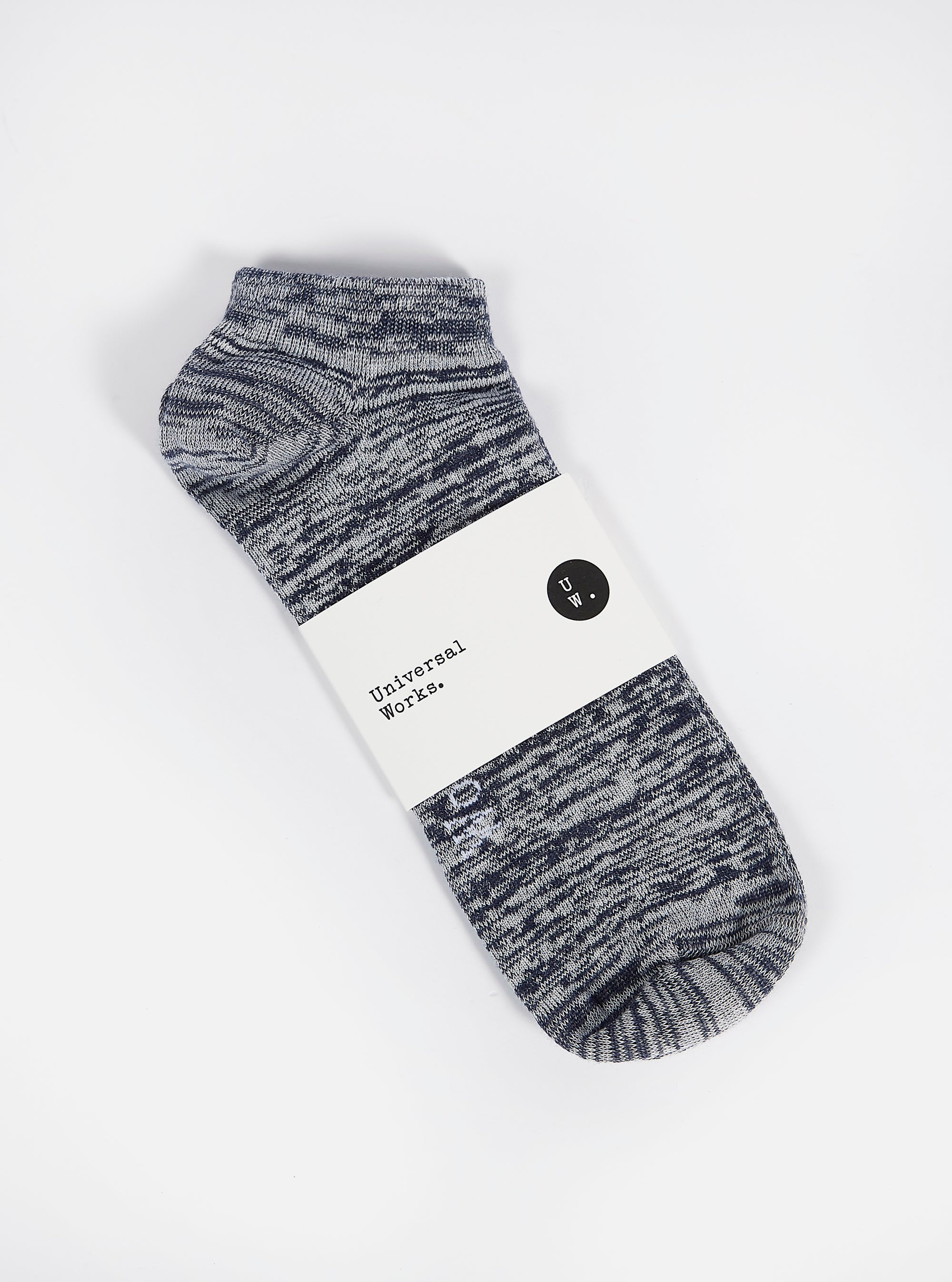 The Navy Slub Knit Ankle Slub Sock, packaged on a white surface. The sock is navy and white knit, with a paper label around it. 
